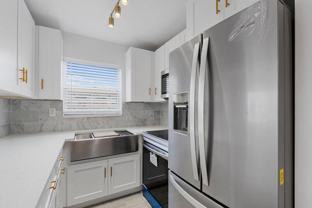 kitchen featuring rail lighting, tasteful backsplash, stainless steel appliances, and white cabinetry