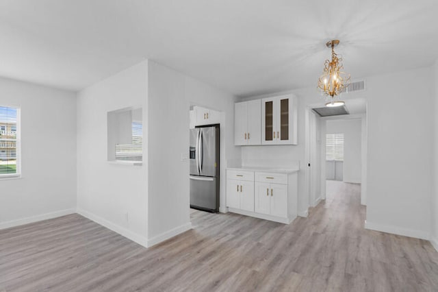 kitchen with hanging light fixtures, stainless steel fridge, white cabinetry, and light hardwood / wood-style floors