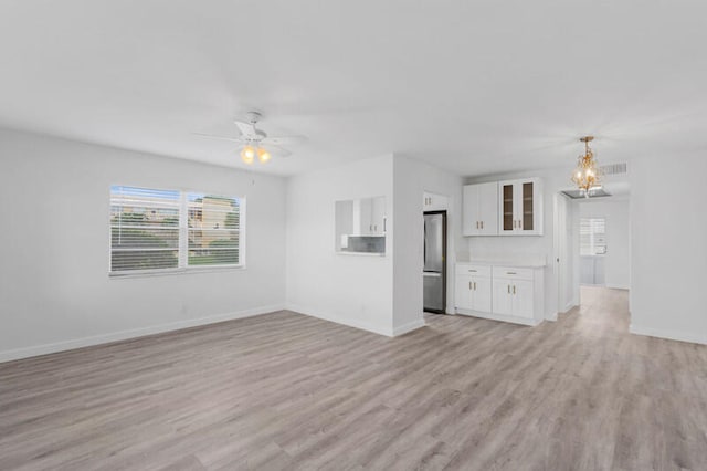 unfurnished living room featuring light wood-type flooring and ceiling fan with notable chandelier