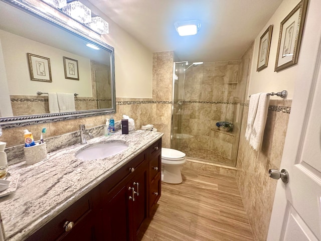 bathroom with vanity, tile walls, wood-type flooring, a shower with door, and toilet