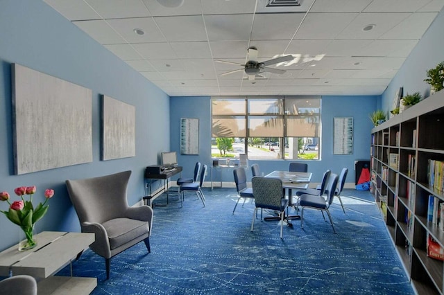 interior space featuring a paneled ceiling, dark colored carpet, and ceiling fan