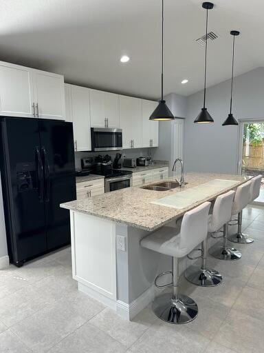 kitchen with visible vents, white cabinets, light stone counters, appliances with stainless steel finishes, and a sink