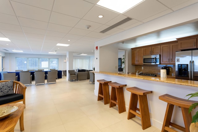 kitchen featuring light stone countertops, backsplash, a breakfast bar area, a paneled ceiling, and appliances with stainless steel finishes