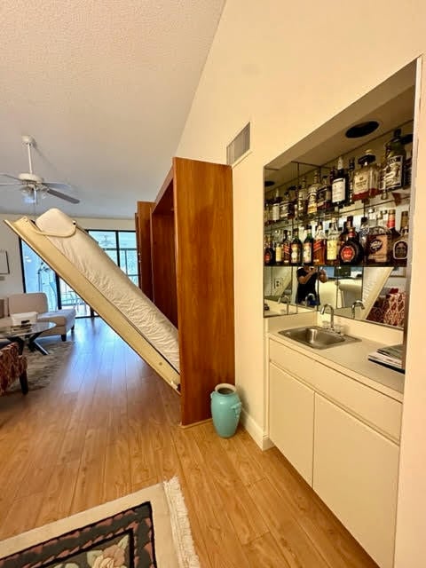 bar with ceiling fan, light wood-type flooring, white cabinets, sink, and a textured ceiling