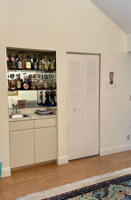 bar featuring sink, light hardwood / wood-style flooring, and lofted ceiling