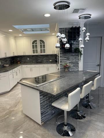 kitchen with decorative backsplash, white cabinetry, hanging light fixtures, a kitchen breakfast bar, and electric stovetop