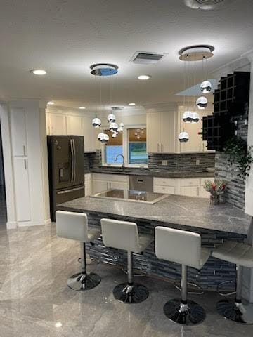 kitchen featuring white cabinetry, black refrigerator, and decorative light fixtures