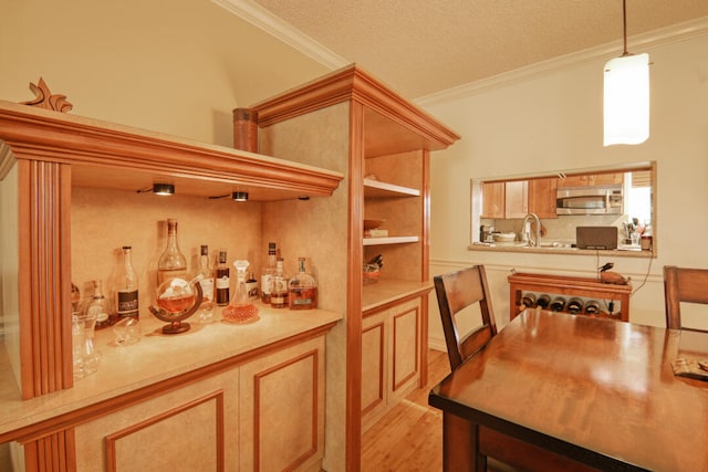 bar with light hardwood / wood-style floors, a textured ceiling, crown molding, decorative light fixtures, and sink