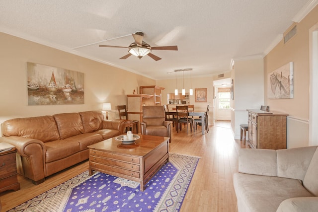 living room with ornamental molding, light hardwood / wood-style floors, ceiling fan, and a textured ceiling