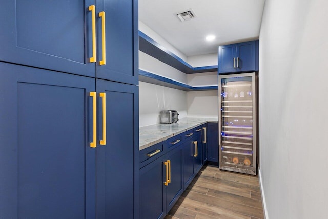 kitchen with wine cooler, blue cabinetry, light stone counters, and dark wood-type flooring