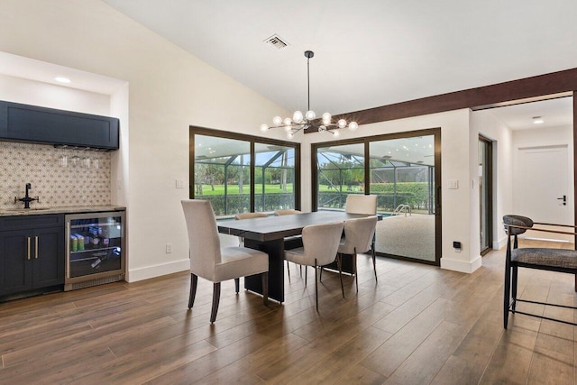 dining area featuring dark hardwood / wood-style flooring, a healthy amount of sunlight, a chandelier, wine cooler, and lofted ceiling