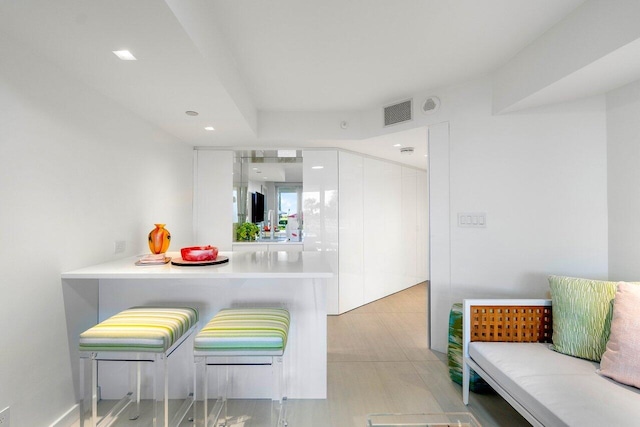 kitchen with kitchen peninsula, a kitchen bar, white cabinets, and light hardwood / wood-style flooring