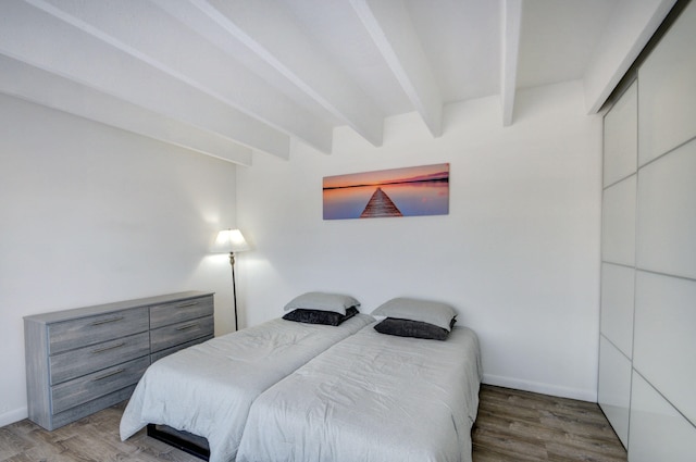 bedroom with beamed ceiling, wood-type flooring, and a closet