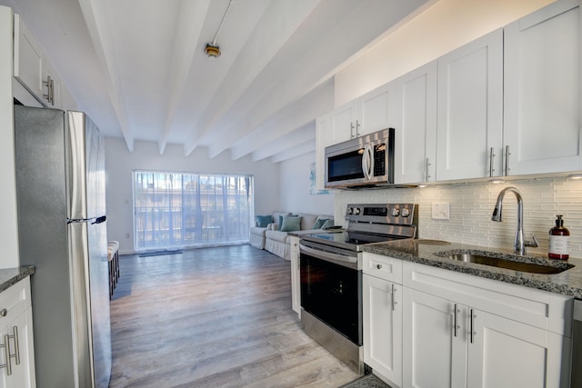 kitchen with stainless steel appliances, sink, dark stone countertops, and beam ceiling