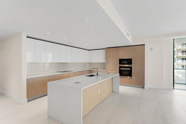 kitchen with an island with sink, modern cabinets, light countertops, black appliances, and white cabinetry