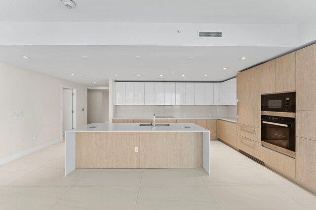 kitchen with light tile patterned floors, a kitchen island with sink, black microwave, wall oven, and sink