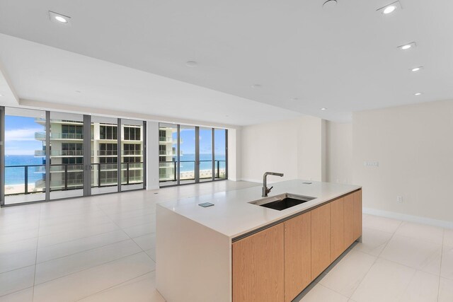 kitchen with sink, expansive windows, light tile patterned floors, and an island with sink