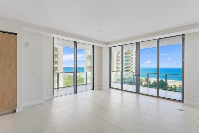 unfurnished room with floor to ceiling windows, a water view, baseboards, and light tile patterned flooring