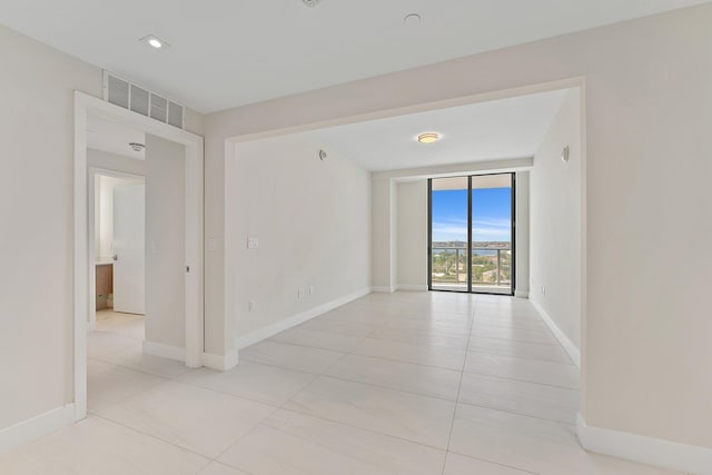 spare room featuring floor to ceiling windows, visible vents, baseboards, and light tile patterned flooring