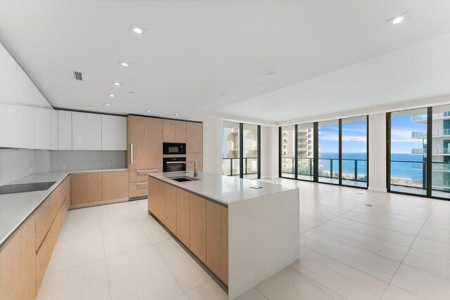 kitchen with floor to ceiling windows, white cabinets, oven, light tile patterned floors, and a kitchen island with sink