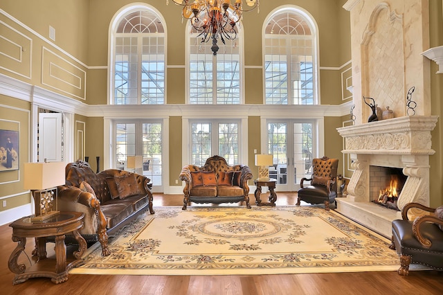 living room with a fireplace, a towering ceiling, wood-type flooring, and an inviting chandelier