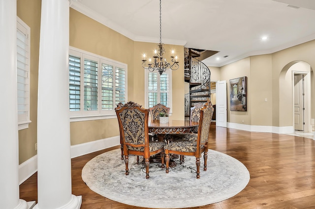 dining space with ornate columns, an inviting chandelier, ornamental molding, and hardwood / wood-style flooring