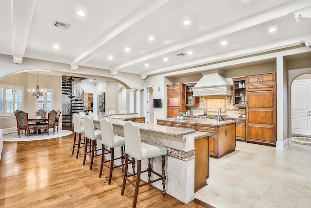 kitchen featuring light stone countertops, light hardwood / wood-style flooring, premium range hood, a spacious island, and a kitchen bar