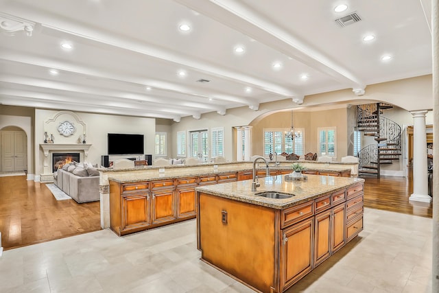 kitchen with beam ceiling, a large island with sink, sink, and light hardwood / wood-style flooring