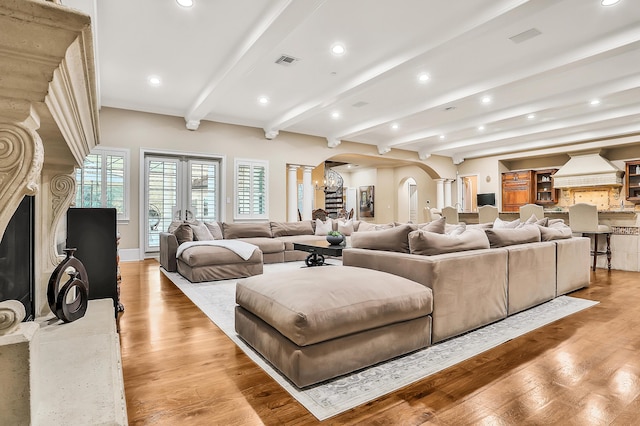 living room featuring beam ceiling, french doors, decorative columns, a chandelier, and light wood-type flooring