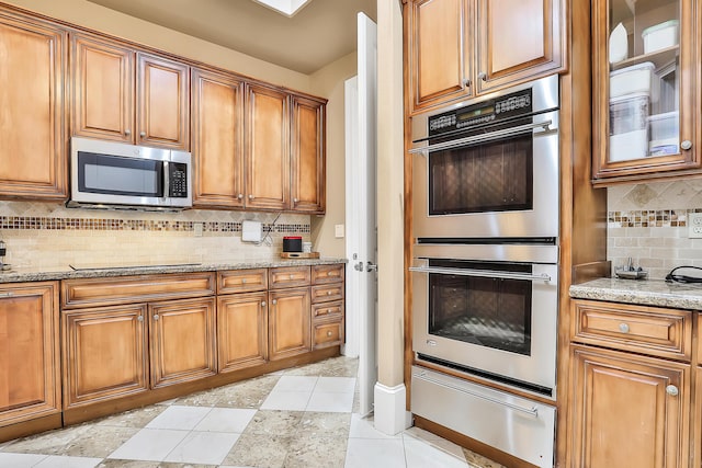 kitchen with light tile patterned floors, backsplash, stainless steel appliances, and light stone counters