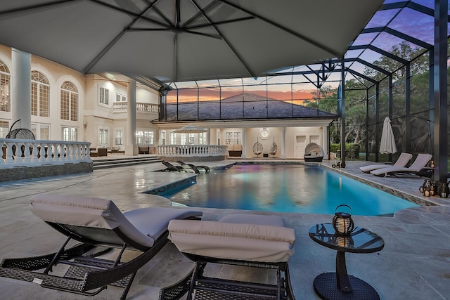 pool at dusk featuring glass enclosure and a patio area