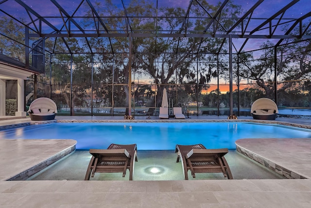 pool at dusk featuring a lanai and a patio