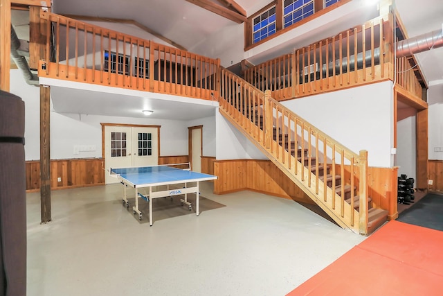 game room featuring high vaulted ceiling, wooden walls, and french doors