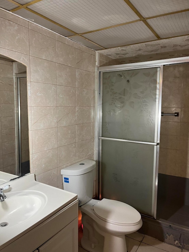 bathroom featuring toilet, tile patterned floors, a shower with door, vanity, and tile walls