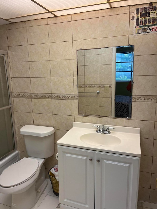 full bathroom featuring toilet, tile patterned floors, vanity, bath / shower combo with glass door, and tile walls