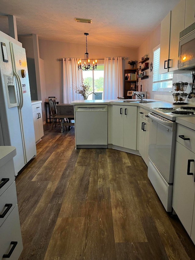 kitchen with pendant lighting, white appliances, dark wood-type flooring, an inviting chandelier, and kitchen peninsula