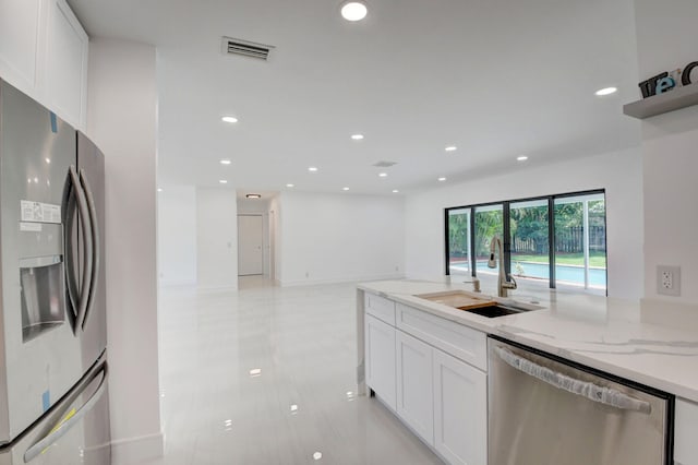 kitchen featuring light stone countertops, sink, light tile patterned floors, white cabinets, and appliances with stainless steel finishes