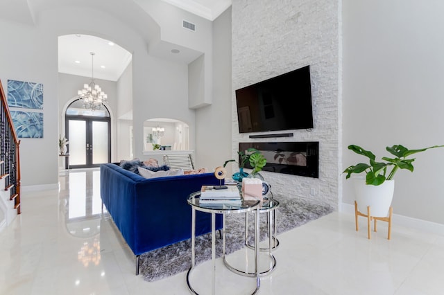 living room with a chandelier, light tile floors, french doors, a stone fireplace, and crown molding