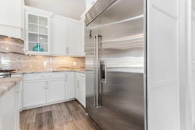 kitchen featuring light stone countertops, white cabinetry, backsplash, built in refrigerator, and light hardwood / wood-style flooring