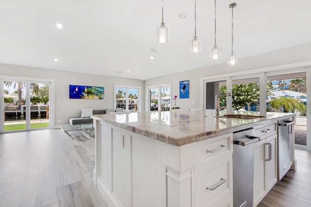 kitchen featuring an island with sink, pendant lighting, light hardwood / wood-style flooring, light stone countertops, and white cabinetry