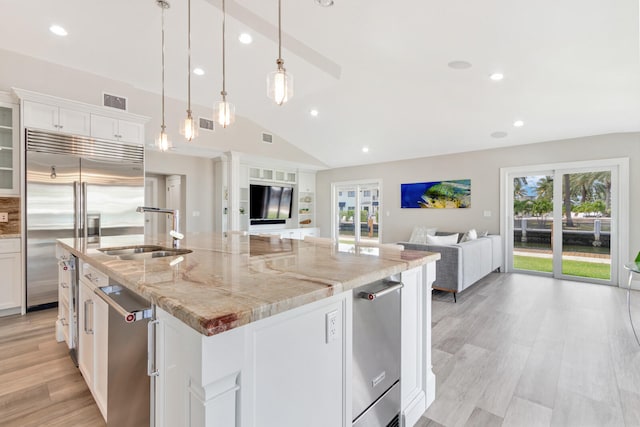 kitchen with a kitchen island with sink, sink, light stone counters, white cabinets, and light hardwood / wood-style flooring