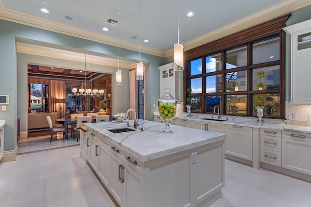 kitchen with white cabinetry, sink, decorative backsplash, hanging light fixtures, and a kitchen island with sink