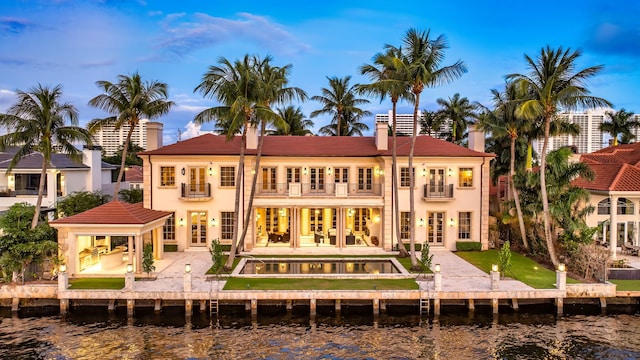 back house at dusk with a pool with hot tub, a balcony, a patio area, and a water view