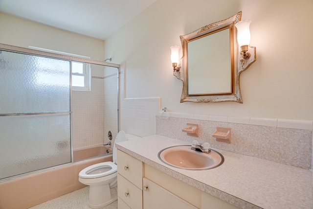 full bathroom featuring tile walls, oversized vanity, backsplash, toilet, and shower / bath combination with glass door