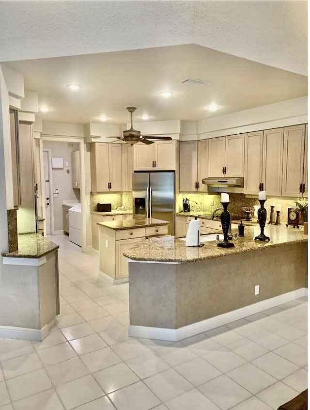 kitchen featuring ceiling fan, light stone counters, stainless steel fridge with ice dispenser, and washer and dryer