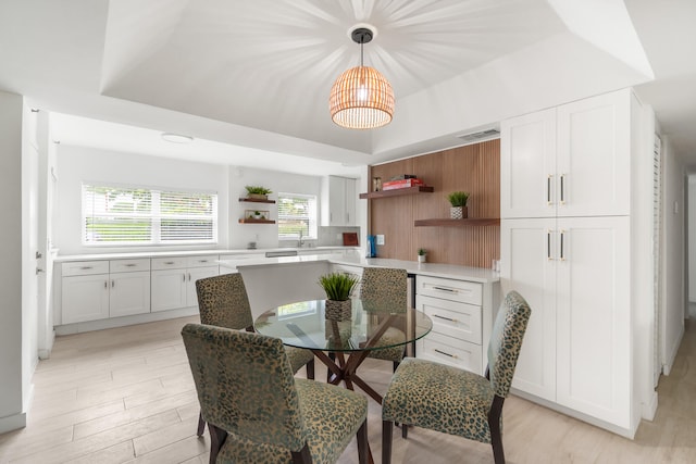 dining space with sink, a tray ceiling, and light wood-type flooring