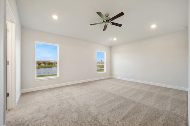 empty room featuring light carpet, a water view, and ceiling fan