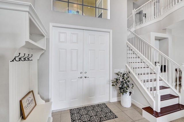 tiled foyer featuring stairway, a towering ceiling, and baseboards