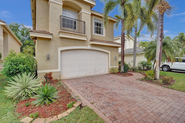 view of front of house featuring a garage, stucco siding, a balcony, decorative driveway, and a tiled roof