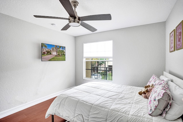 bedroom featuring wood finished floors, baseboards, a ceiling fan, and a textured wall
